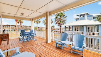 Um deck coberto ao ar livre com piso de madeira, cadeiras Adirondack azuis e uma mesa.
