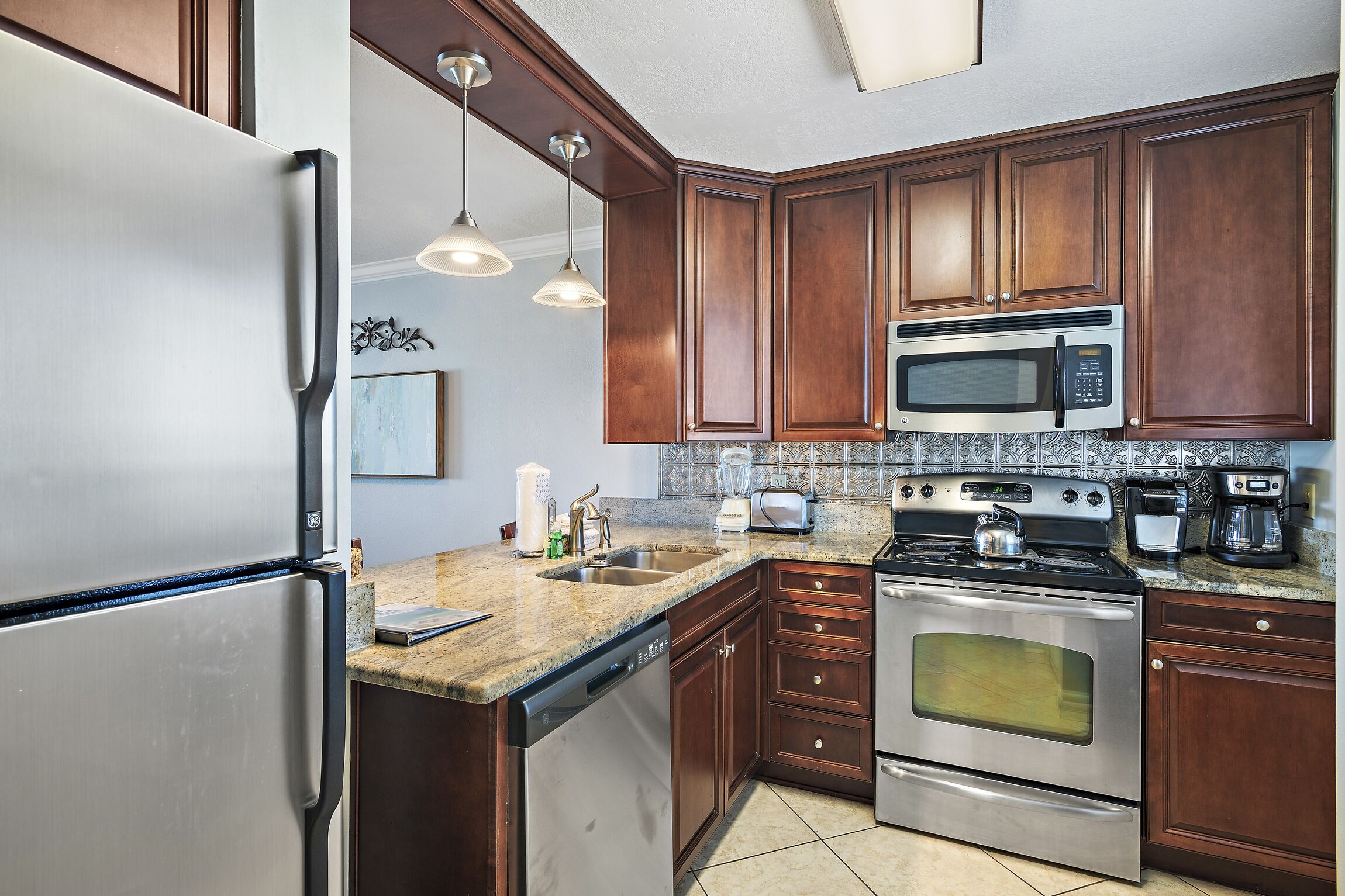 A kitchen with stainless steel appliances, wooden cabinets, a granite countertop, and pendant lighting.
