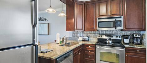 A kitchen with stainless steel appliances, wooden cabinets, a granite countertop, and pendant lighting.