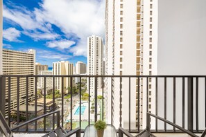 Un balcon offrant une vue sur des immeubles de grande hauteur et une piscine située en contrebas.