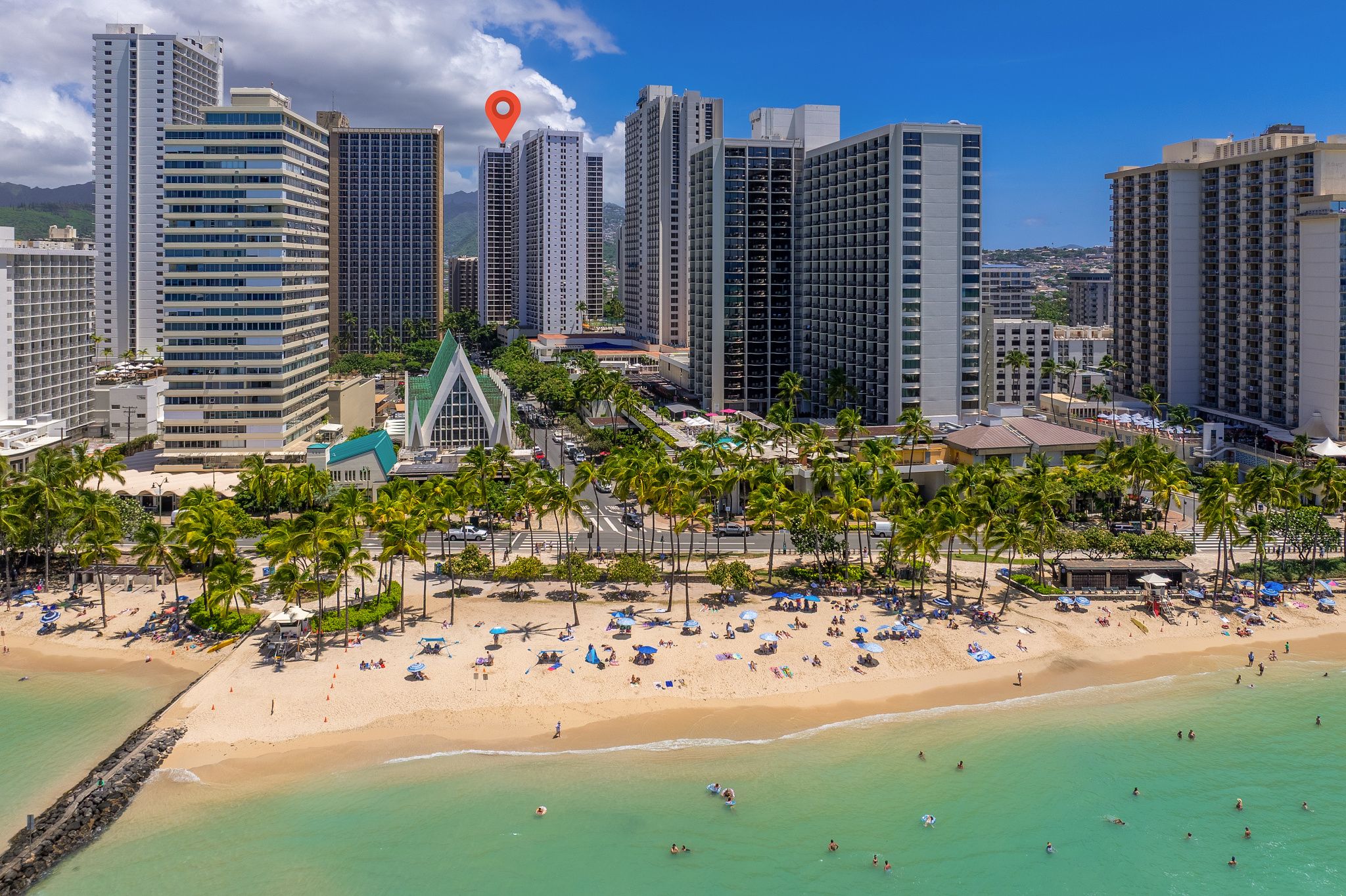 A coastal cityscape with high-rise buildings, a beach with umbrellas, and palm trees.
