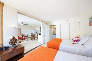 Quarto de hotel com duas camas, uma escrivaninha com candeeiro, uma cadeira e vista para a sala de jantar.