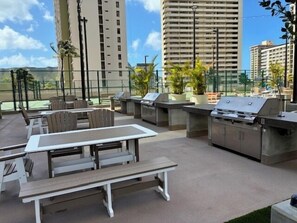 Um pátio externo com mesa, cadeiras, churrasqueira e vista para edifícios altos.