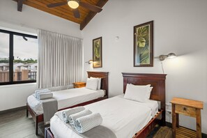 Une chambre d’hôtel avec deux lits, un ventilateur de plafond, une fenêtre avec des rideaux et des œuvres d’art accrochées aux murs.