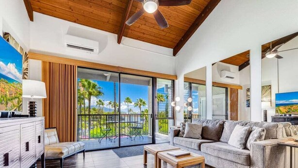 A spacious living room with a large sofa, a coffee table, and a view of palm trees through large sliding glass doors. - Roomy Maui Suite w/Loft, Relaxing Lanai, Kitchen Ease, WiFi–Kamaole Sands 10408 (KIHEI)