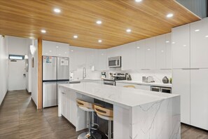 A modern kitchen with white cabinetry, a marble island, and stainless steel appliances. - Roomy Maui Suite w/Loft, Relaxing Lanai, Kitchen Ease, WiFi–Kamaole Sands 10408 (KIHEI)