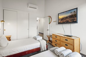 Quarto de hotel com cama, cômoda, televisão e espelho fixado na parede.