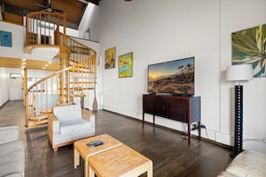 Uma sala de estar ampla com escada de madeira, TV de tela plana e obras de arte nas paredes.