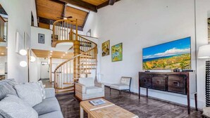 A spacious living area with a wooden staircase, a large flat-screen TV, and a sofa. - Roomy Maui Suite w/Loft, Relaxing Lanai, Kitchen Ease, WiFi–Kamaole Sands 10408 (KIHEI)