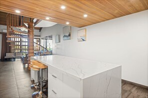 Une cuisine moderne avec un plan de travail en marbre, un plafond en bois et un escalier menant à un niveau supérieur.