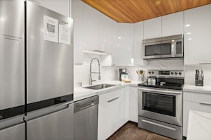 Cozinha moderna com eletrodomésticos de aço inoxidável, micro-ondas, forno e lava-louças.