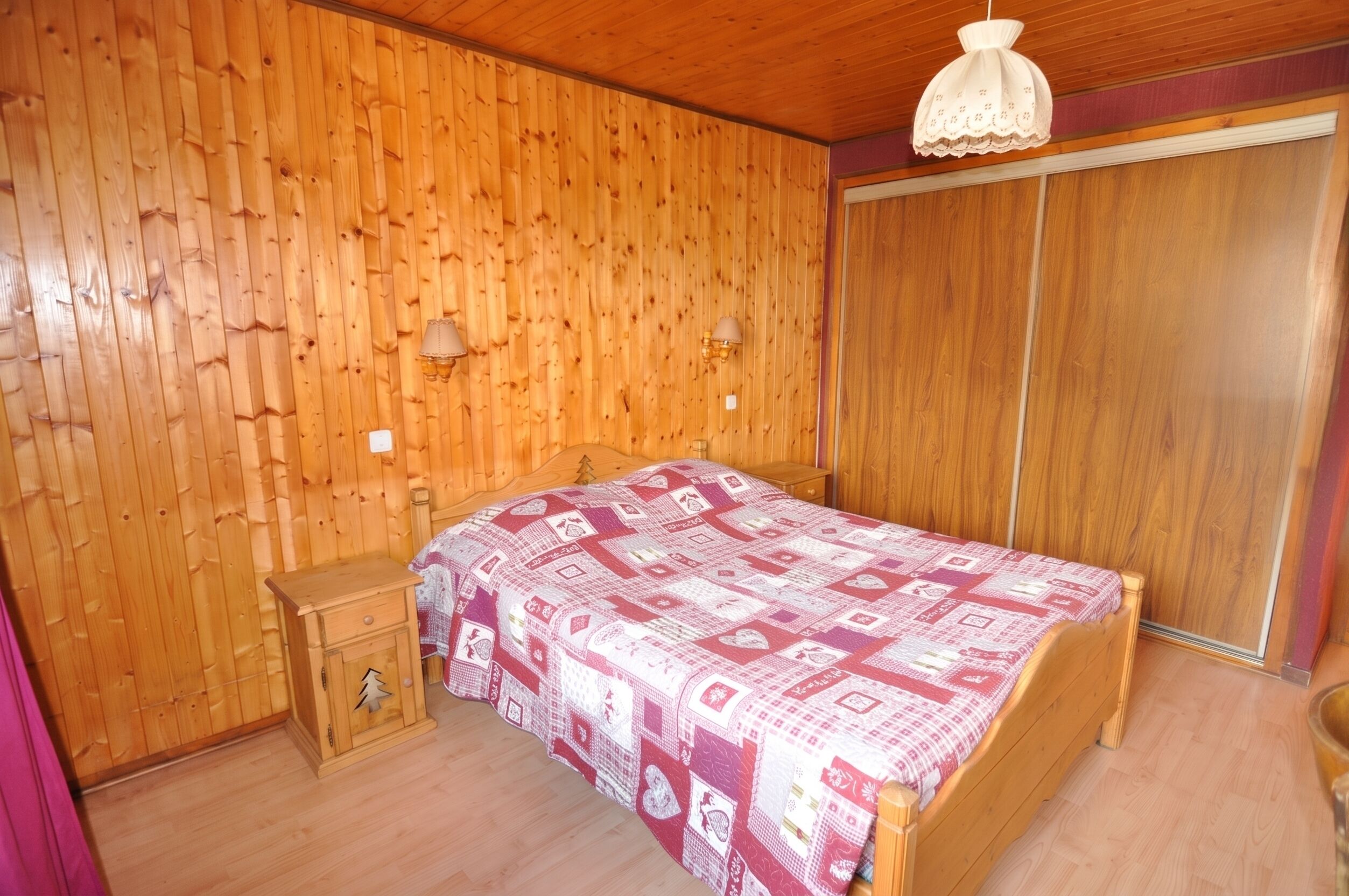 A wooden-paneled room with a bed, bedside table, and a wardrobe.