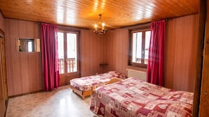 Una habitación con paredes y techo de madera, dos camas con ropa de cama estampada, un espejo y una araña.