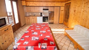 Un interior de madera con cocina, una mesa de comedor con mantel rojo, un sofá y un televisor.