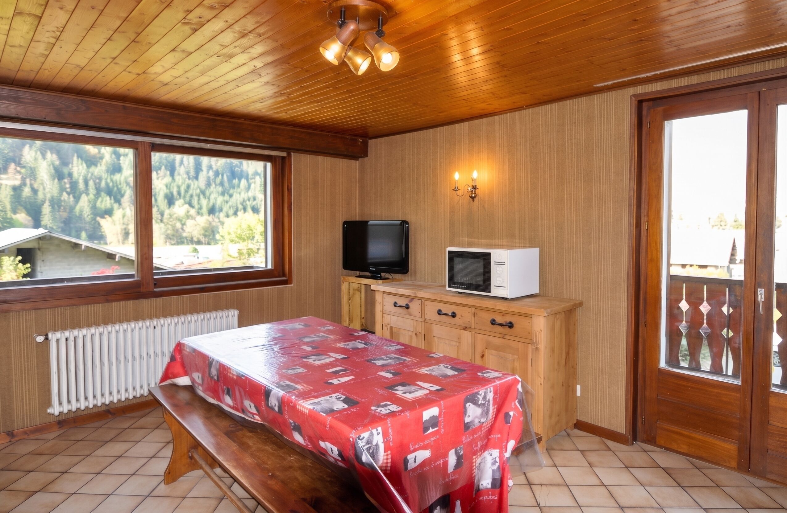 Ein Zimmer mit Holzwänden, einem Bett, einem Tisch, einem Fernseher und einer Mikrowelle.