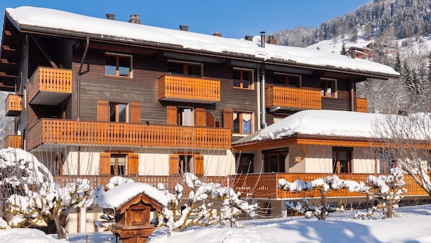Una cabaña de varios pisos con balcones, una valla de madera y paisajes nevados.