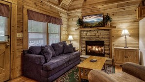 A cozy cabin interior with a stone fireplace, wooden walls, a comfortable sofa, and a television mounted above the fireplace.