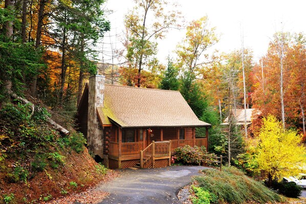 A rustic cabin with a stone chimney, wooden deck, and a porch.