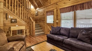 A wooden cabin interior with a staircase, a sofa, a chair, and a table.