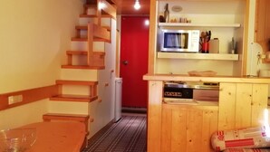 A wooden interior with a staircase, a red door, and a kitchen area with a microwave and stove.