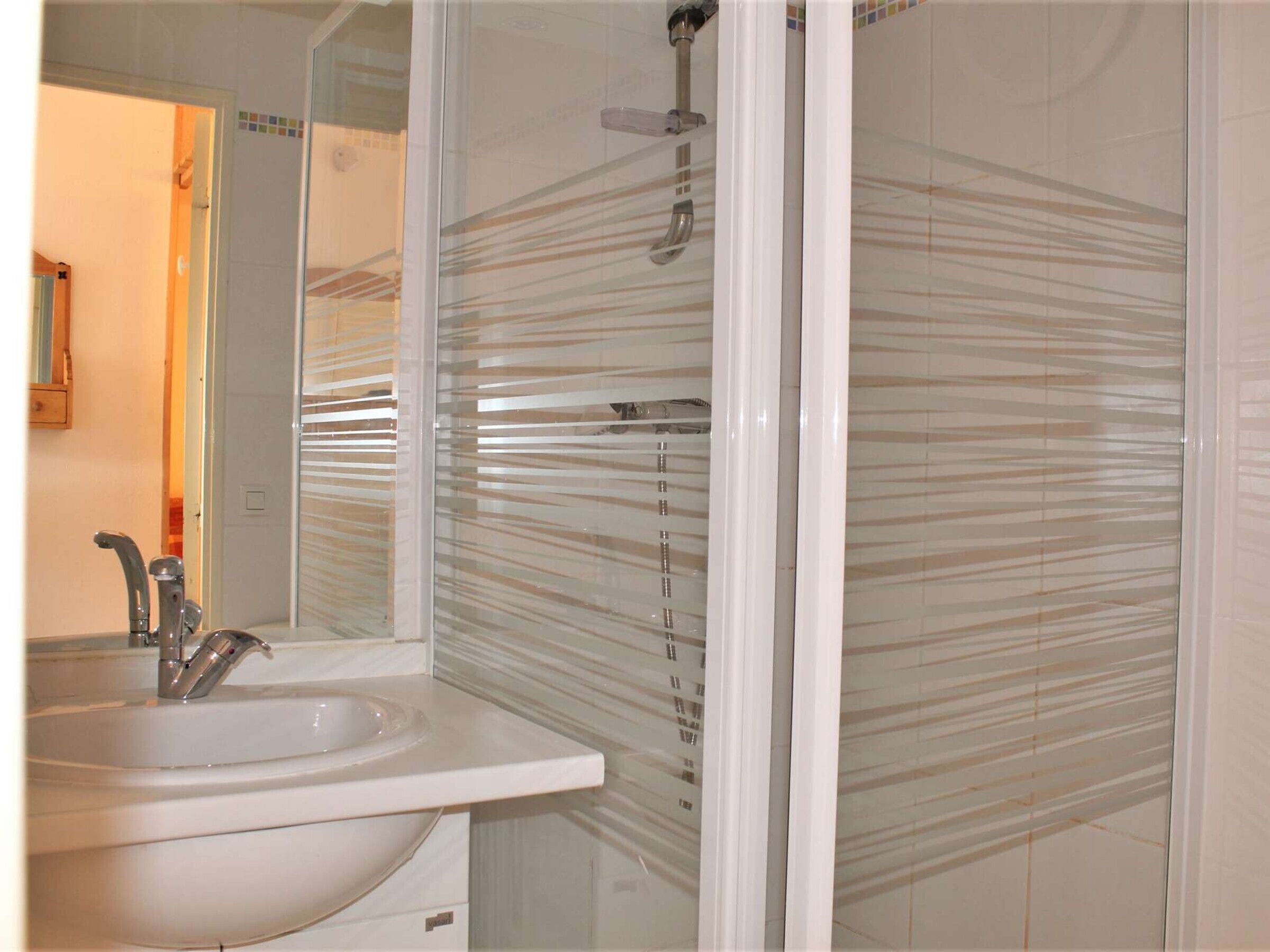 A bathroom with a glass shower enclosure, a sink with a modern faucet, and a mirror.