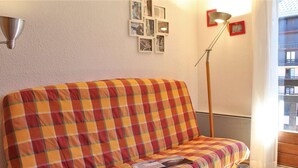 Una habitación acogedora con un sofá a cuadros, una pequeña mesa de madera con una taza, y una lámpara de pie.