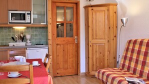 Una cocina compacta con microondas, cafetera y una mesa de comedor con sillas. Hay un armario de madera y un sofá de cuadros en la sala de estar.
