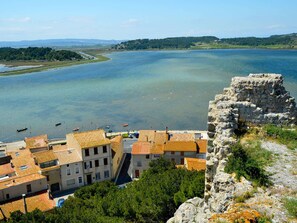 A coastal town with terracotta-roofed buildings, a clear blue sea, and a stone ruin.