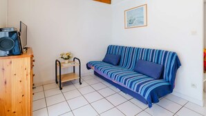 A cozy living room with a blue-striped sofa, wooden beams on the ceiling, a small table with a vase, and a framed picture on the wall. - 2-Room Pavilion + Mezzanine for 5, Terrace (Gruissan)