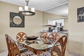 A dining area with a glass table surrounded by wicker chairs, a decorative mirror, and a modern chandelier. - π΄ Welcome to Islander #105 β Your Fun & Relaxing Beach Escape! π
(Destin)