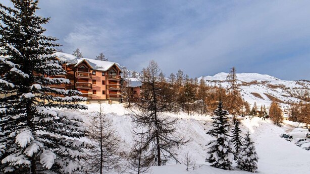 A lodge with multiple balconies, surrounded by snow-covered trees and mountains.