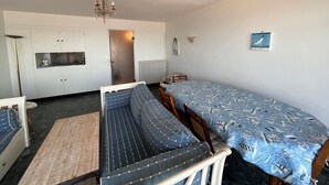 Una habitación funcional con cama, una mesita, kitchenette y lámpara de araña.