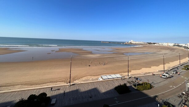 Una playa con un paseo marítimo, un muelle y edificios al fondo.