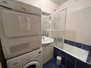 A compact bathroom with a washing machine, a sink, a mirror, and a bathtub.