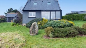 A modern two-story house with a sloped roof, large windows, and a well-maintained garden with a rock, bushes, and yellow flowers. - Renovated house with garden, wifi, BBQ, parking, 250m from the sea - Pleumeur-Bodou (Pleumeur-Bodou)
