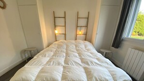 A neatly made bed with a white duvet, two bedside tables, and a window with curtains. - Renovated house with garden, wifi, BBQ, parking, 250m from the sea - Pleumeur-Bodou (Pleumeur-Bodou)