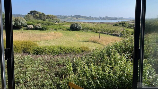 A view through a window of a grassy field with a body of water and trees in the distance. - Renovated house with garden, wifi, BBQ, parking, 250m from the sea - Pleumeur-Bodou (Pleumeur-Bodou)