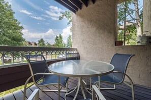 A covered outdoor patio with a round table and two chairs, a railing, and a view of the surrounding area. - TR1104 | Updated Corner Unit | Winter Shuttle | 10 Hot Tubs | Close to Skiing (Steamboat Springs)