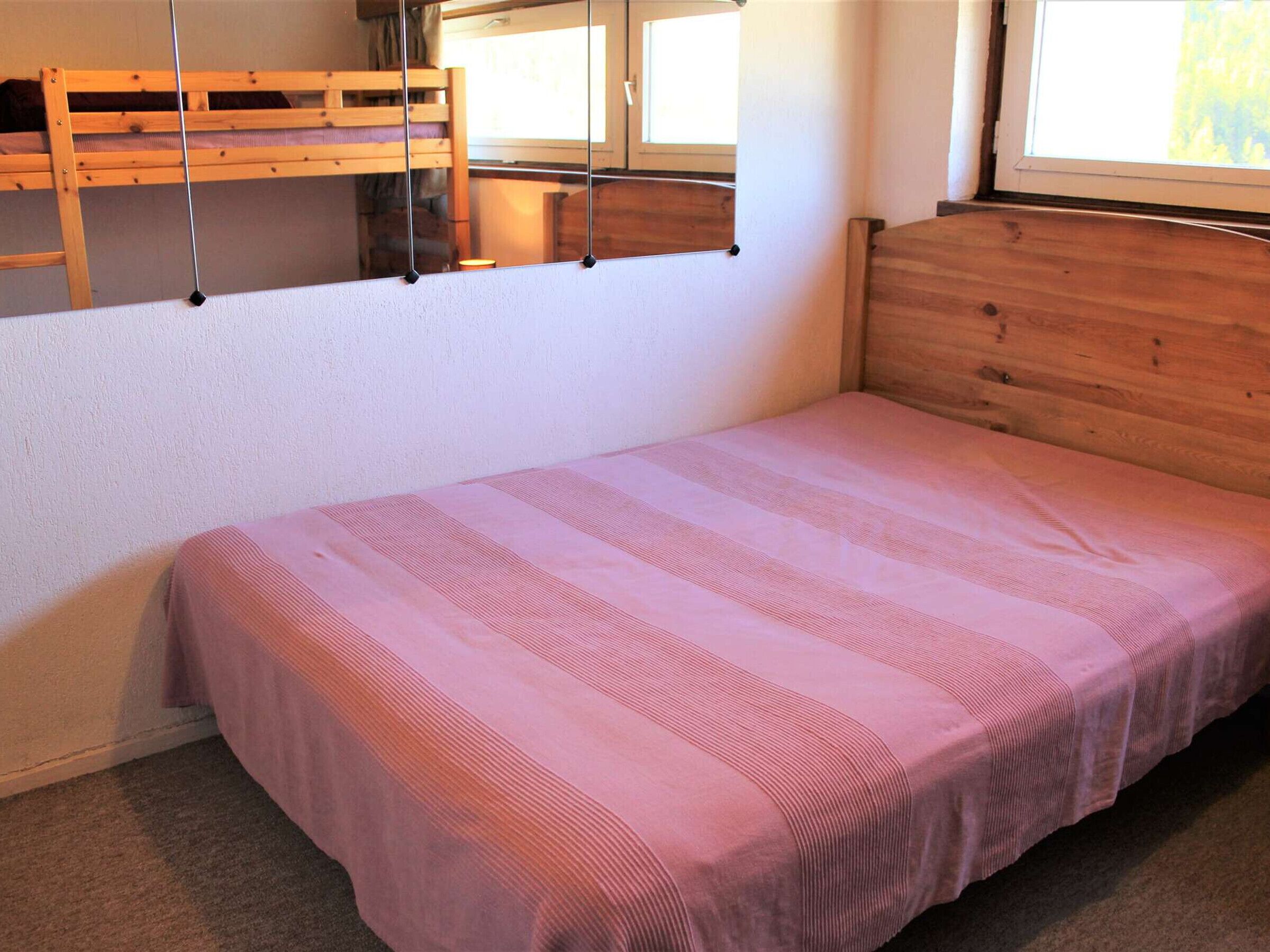 Un lit simple avec une couvre-lit à rayures roses, dans une chambre dotée d’une tête de lit en bois et d’une fenêtre.