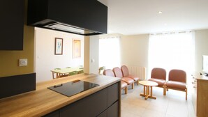 Une cuisine moderne dotée d’une hotte noire, d’un plan de travail en bois et d’une cuisinière intégrée. On y trouve un coin repas avec une table et des chaises, ainsi qu’un coin salon avec un canapé et une petite table ronde.