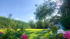 Un jardin doté d’une aire de jeux, comprenant un toboggan et des balançoires, entouré d’une végétation luxuriante et de plantes en fleurs.