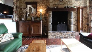 Un salon de style rustique avec une cheminée en pierre, des poutres en bois et un canapé en cuir vert.