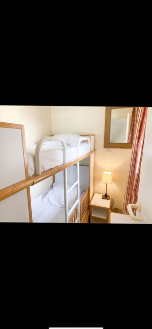 A bunk bed room with a bedside table, lamp, and a mirror.