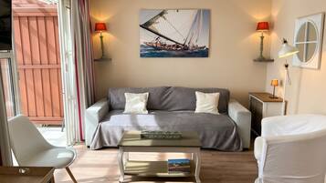 Een moderne woonkamer met een bank, een salontafel en een fauteuil. Aan de muur hangt een schilderij van een zeilboot, en aan beide zijden van de bank staan twee lampen.
