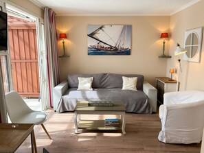 Een moderne woonkamer met een bank, een salontafel en een fauteuil. Aan de muur hangt een schilderij van een zeilboot, en aan beide zijden van de bank staan twee lampen.
