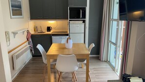 Une cuisine compacte avec un coin repas, comprenant une table avec des chaises, un four à micro-ondes, un réfrigérateur et une fenêtre avec des rideaux.