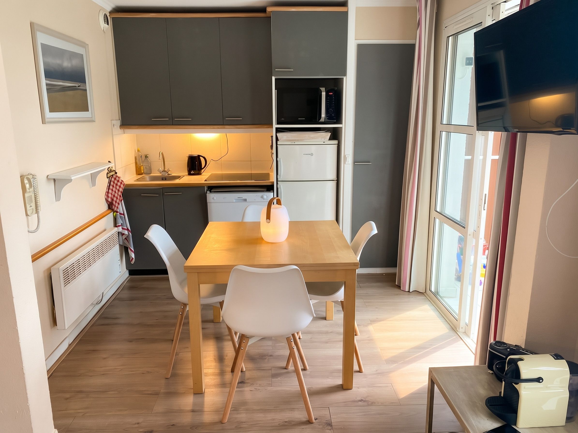 Een kleine keuken met een eettafel, stoelen en een koelkast.