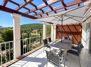A balcony with a table and chairs, a pergola, and a view of a hilly landscape.