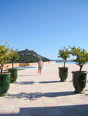 A person standing on a tiled patio with a view of a hill and a body of water.