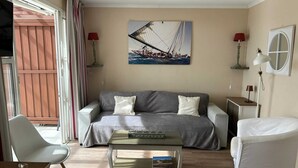 Un salon avec un canapé gris, des fauteuils blancs, une table basse et un tableau représentant un voilier accroché au mur.